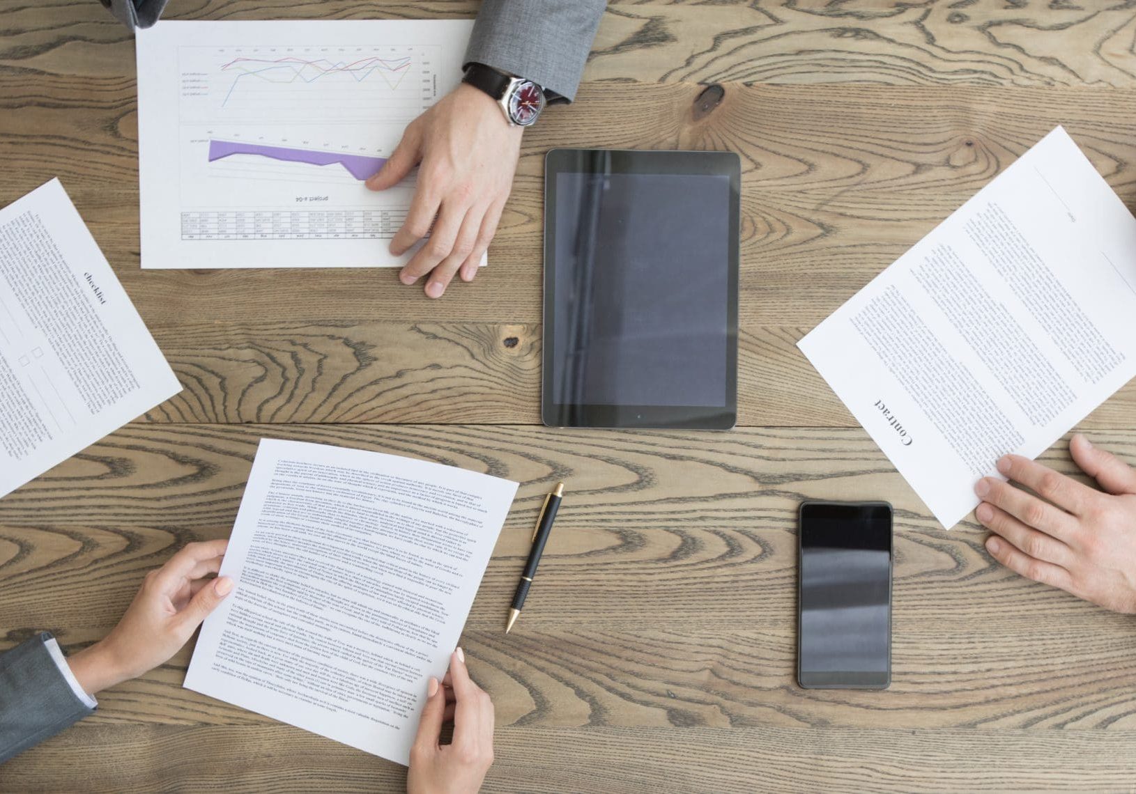 Business people discuss contract sitting around office table, top view
