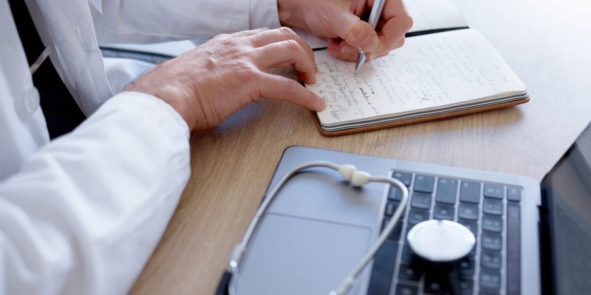 Doctor, writing or hands and notebook, laptop or stethoscope in medical research, ideas or vision in treatment. Zoom, man or healthcare worker and technology, prescription planning or hospital review.